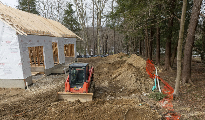 Construction equipment, the frame of a new building, and piles of dirt near a grove of trees