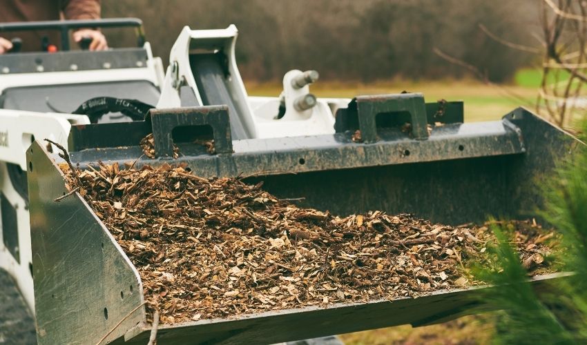 Independent Tree employee moving wood chip mulch with a front loader