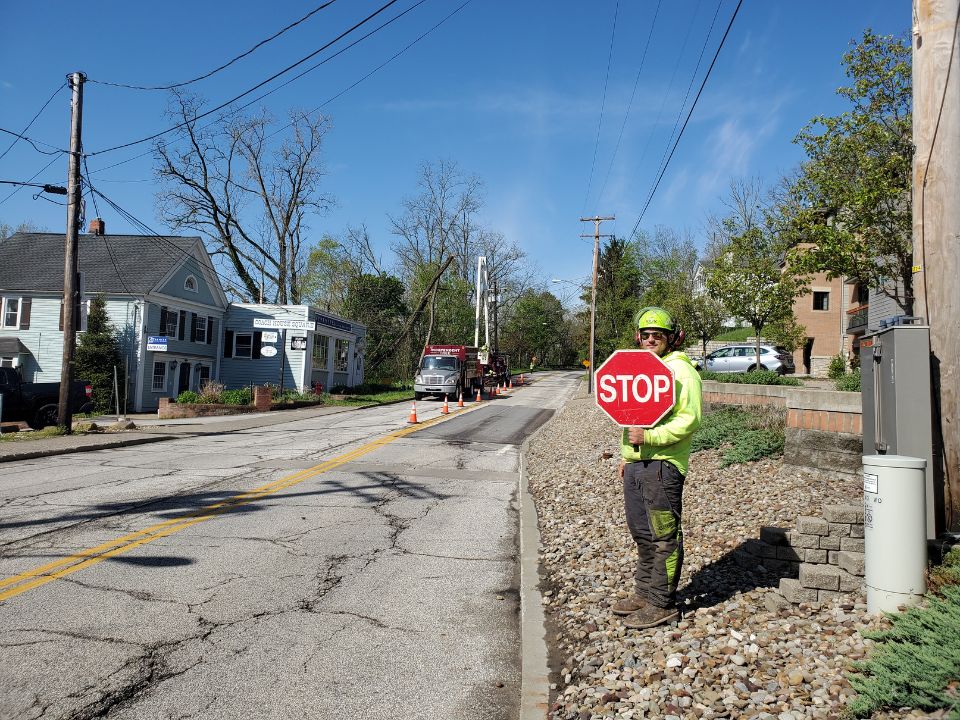 An Indepent Tree worker at the side of the road holding a stop sign.